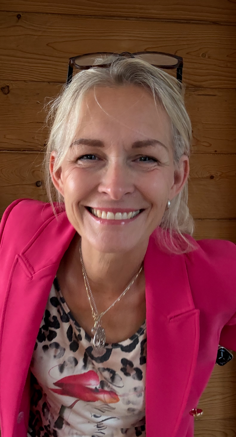 Auf dem Bild sieht man Marion Lang im Profil. Sie strahlt lustig in die Kamera. Sie trägt ihre blonden Haare zu einem Zopf nach hinten gebunden. Sie ist dezent geschminkt. Sie trägt eine Halskette und ein Leoparden Oberteil, da drüber einen pinken Blazer. Im Hintergrund sieht man eine hölzerne Wand.