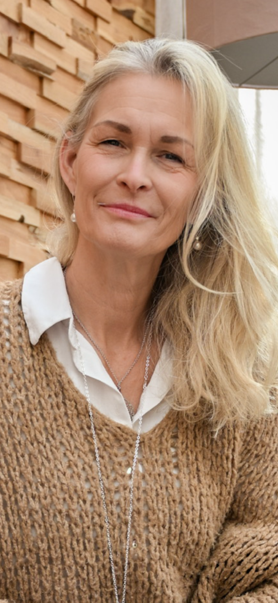 Auf dem Bild sieht man Marion Lang rechts von der Seite. Sie schaut nachdenklich und hat ihren Kopf auf ihre rechte Faust gestützt. Ihre langen blonden Haare liegen auf ihrer rechten Seite ganz locker auf. Im Hintergrund sieht man eine Wohnung wo die Sonne durch die Fenster scheint.